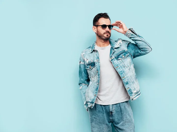 Mężczyzna ubrany w jeansową kurtkę, który stoi na tle błętkitnej ściany