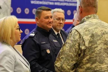 Funkcjonariusz policji w mundurze rozmawia z mężczyzną w kamuflażu podczas spotkania w sali konferencyjnej.