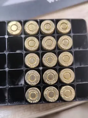 Zbliżenie na czternaście nabojów kalibru 9 mm umieszczonych w czarnej plastikowej skrzynce na amunicję.
